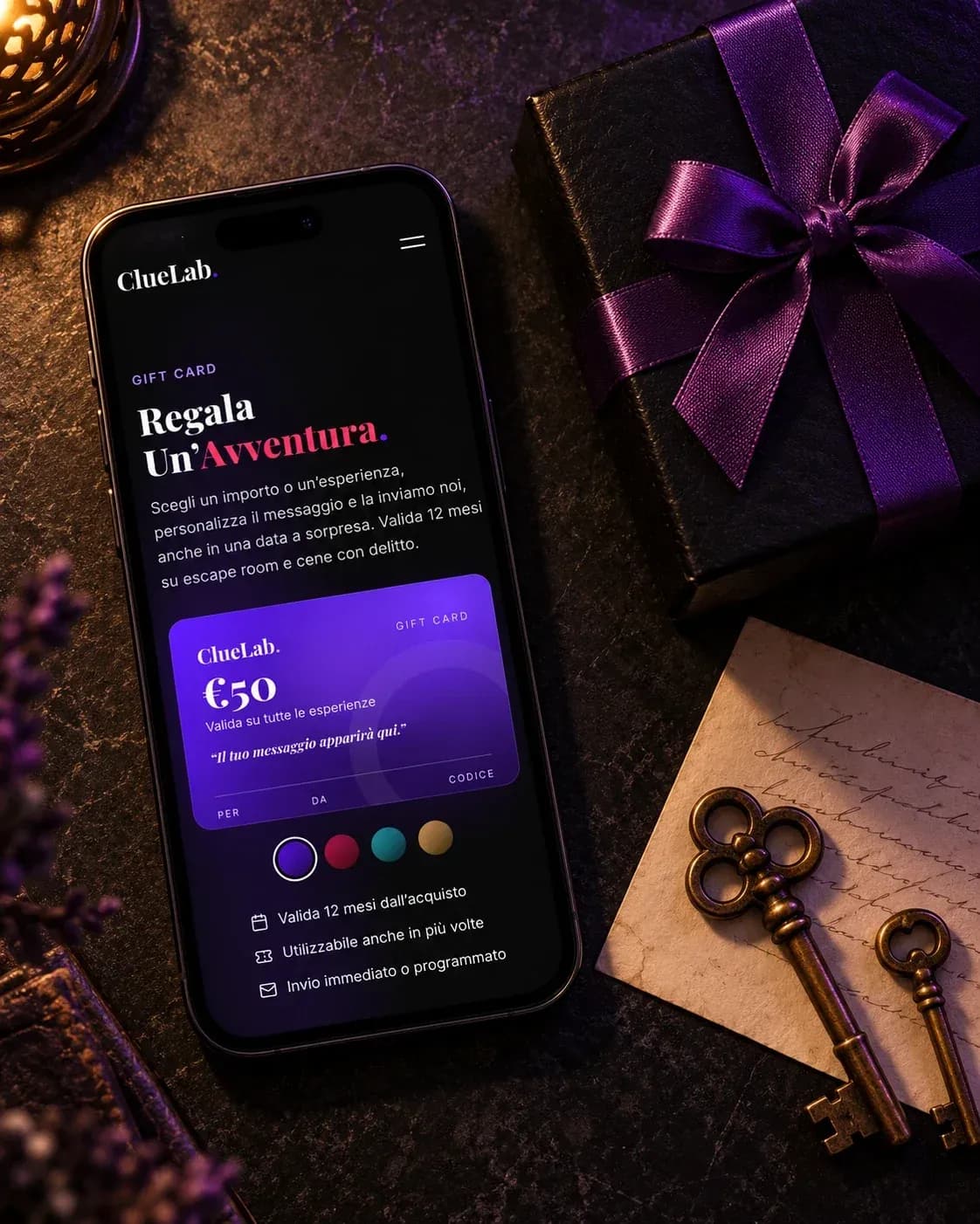 Smartphone con la pagina gift card di ClueLab e la carta viola da 50 euro in anteprima, accanto a un pacchetto regalo con il nastro viola e due chiavi antiche