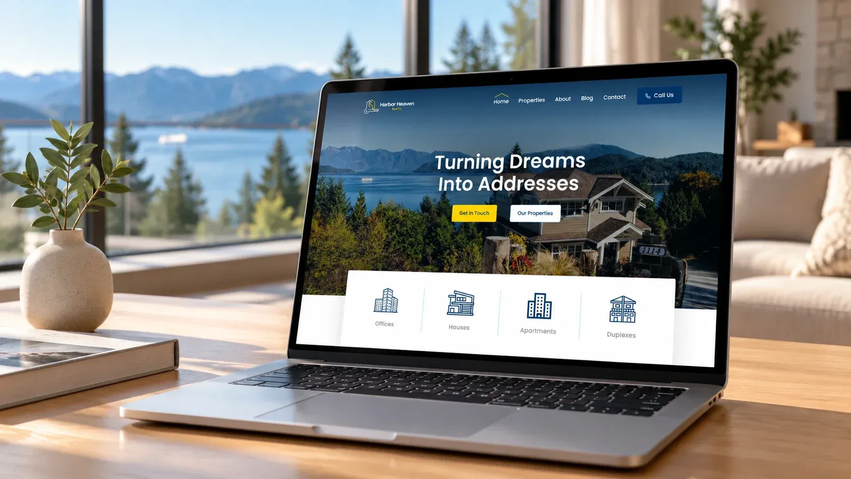 Homepage di Harbor Heaven Realty su un portatile appoggiato su un tavolo di legno, davanti a una vetrata con vista su un lago e sulle montagne