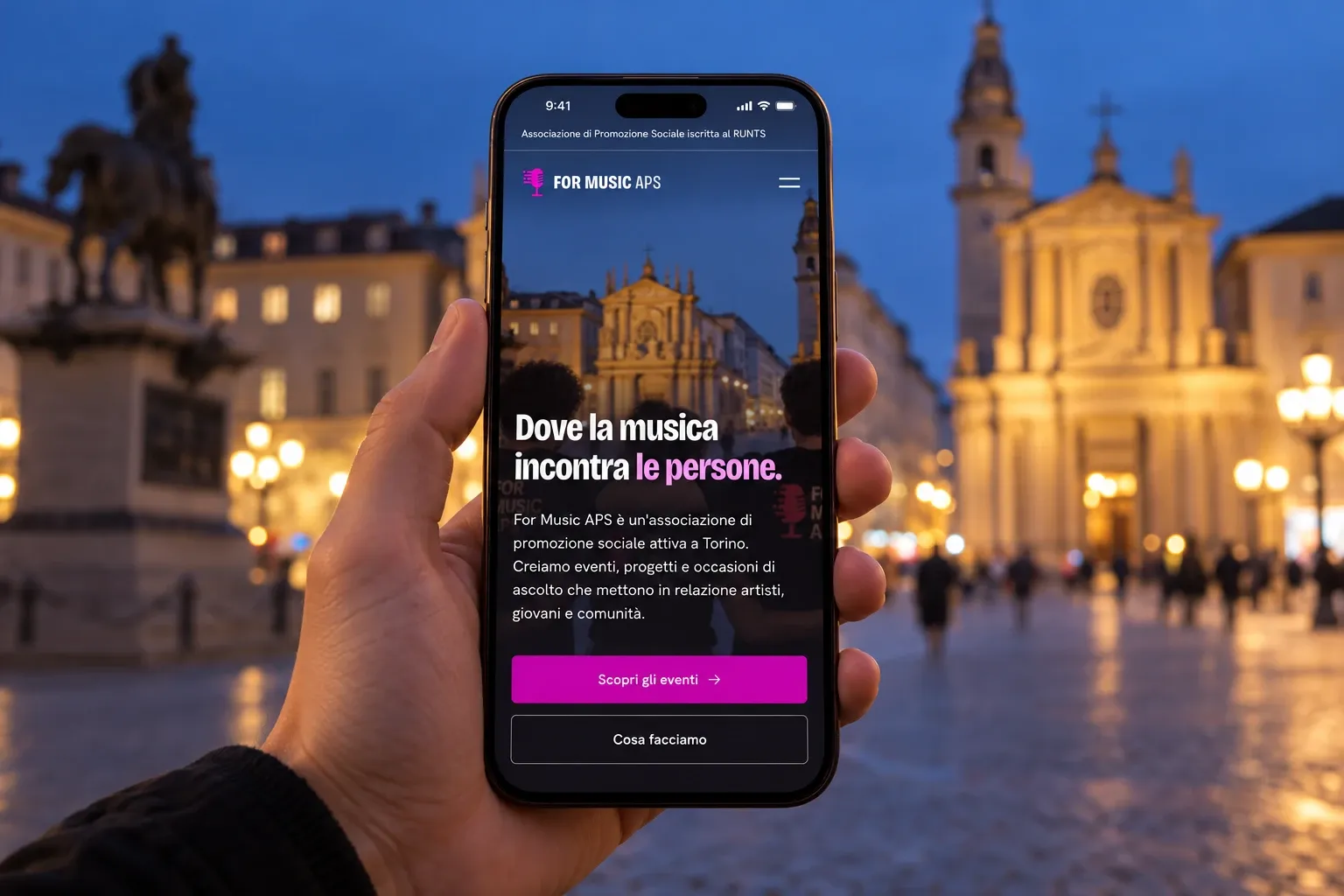 Mano che tiene uno smartphone con la homepage di For Music APS in una piazza di Torino la sera
